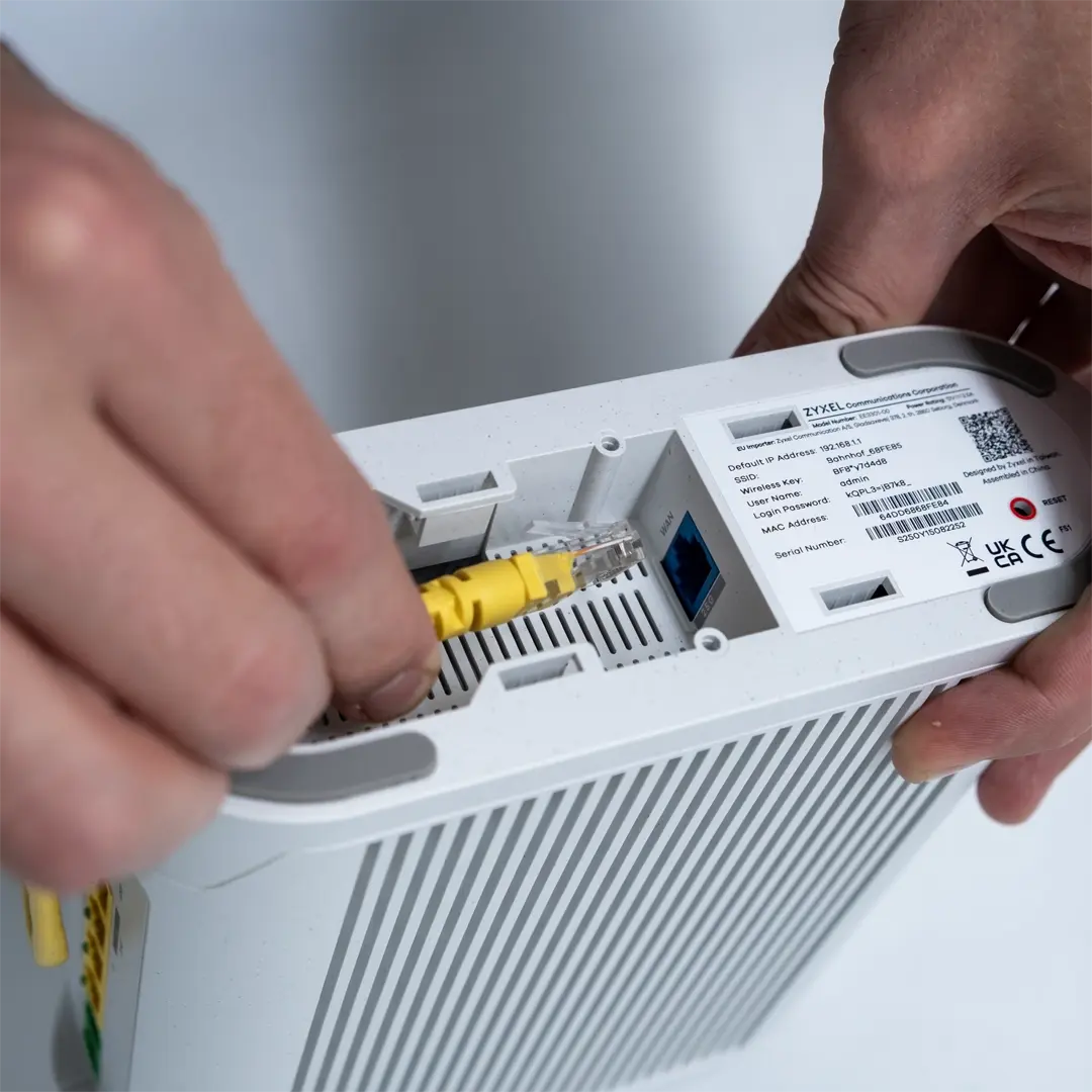 Henkilö liittää keltaisen verkkokaapelin Zyxelin reitittimen pohjassa olevaan porttiin.