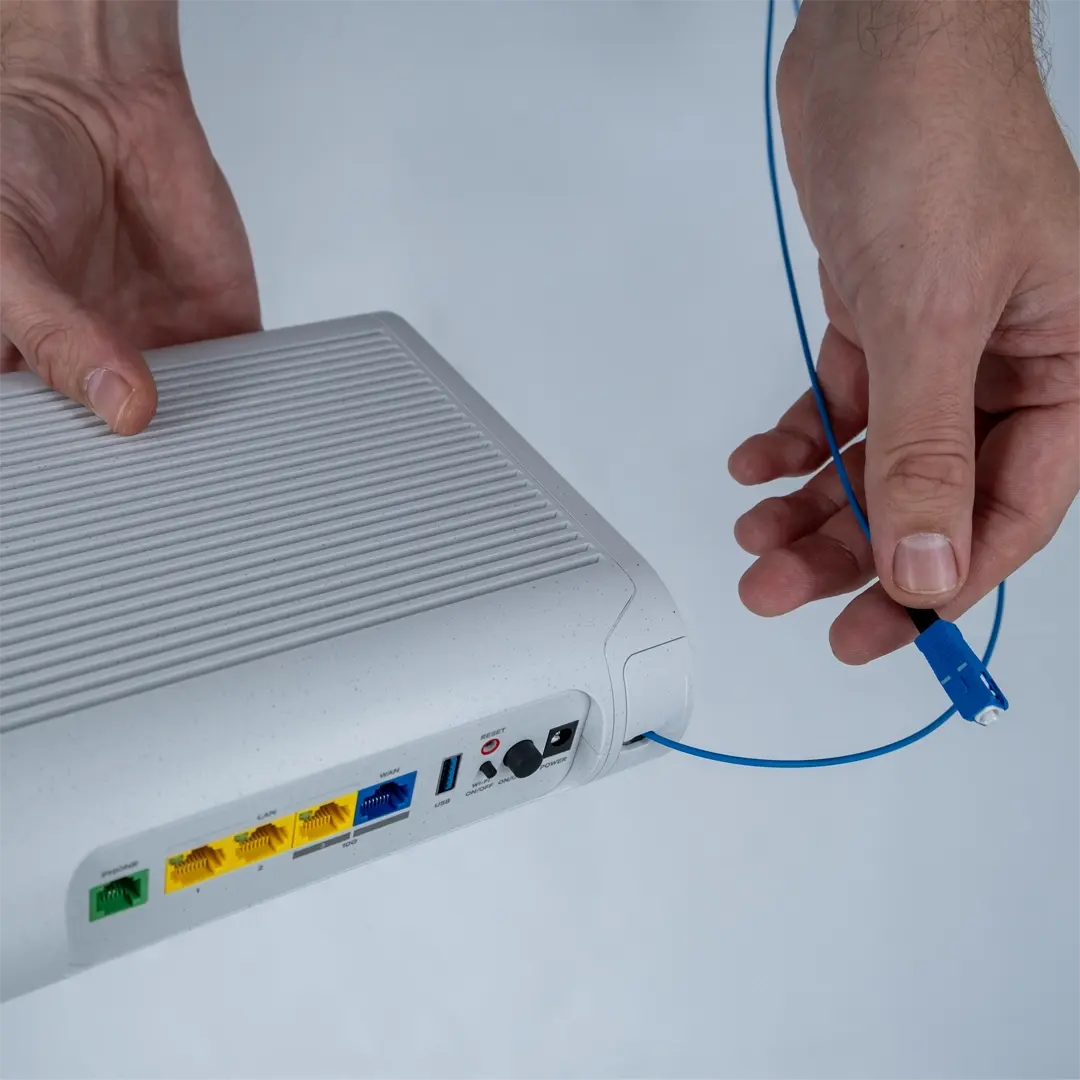Henkilö pitää reititintä ja näyttää sinisen valokuitukaapelin, joka on tarkoitus liittää kodin kuitupistorasiaan.