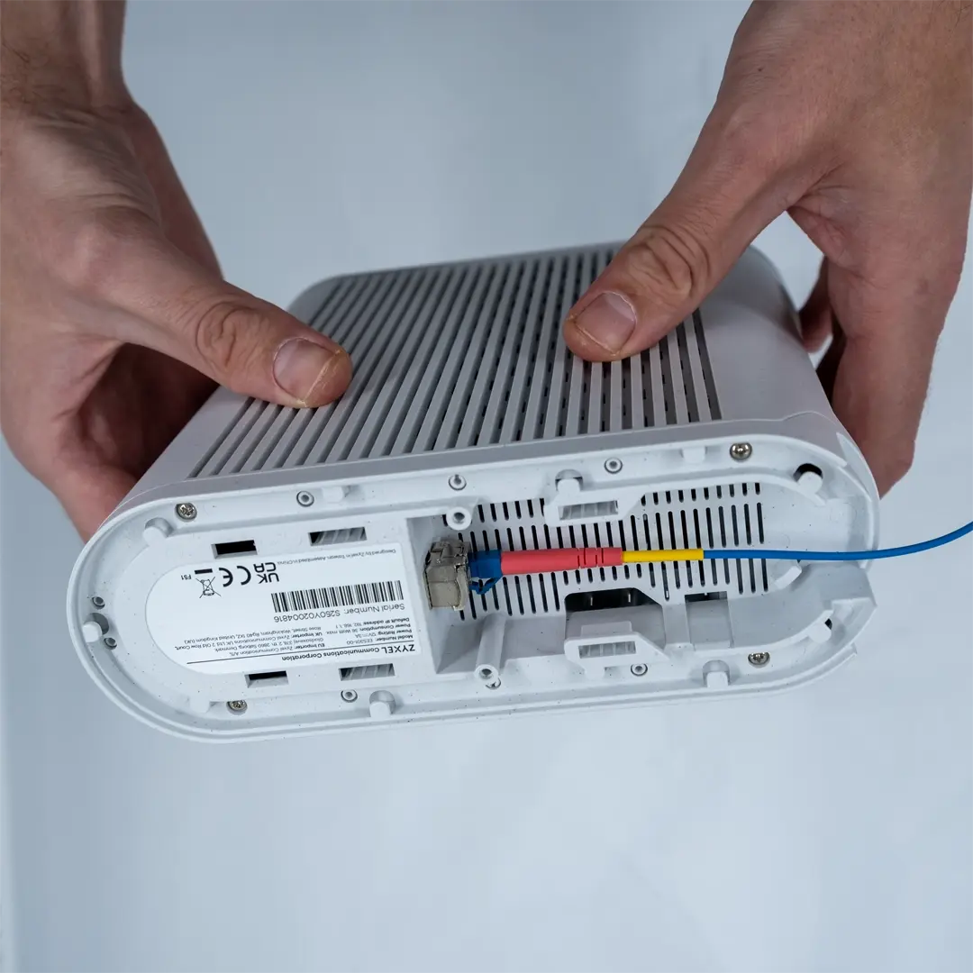 Henkilö pitää reititintä ylösalaisin ja näyttää, kuinka SFP-moduuli, johon on liitetty sininen valokuitukaapeli, on asetettu laitteen pohjassa olevaan liitäntään.