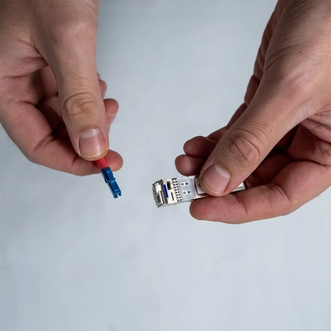 Henkilö pitää SFP-moduulia toisessa kädessä ja näyttää sinisen valokuitukaapelin liitintä toisessa kädessä.