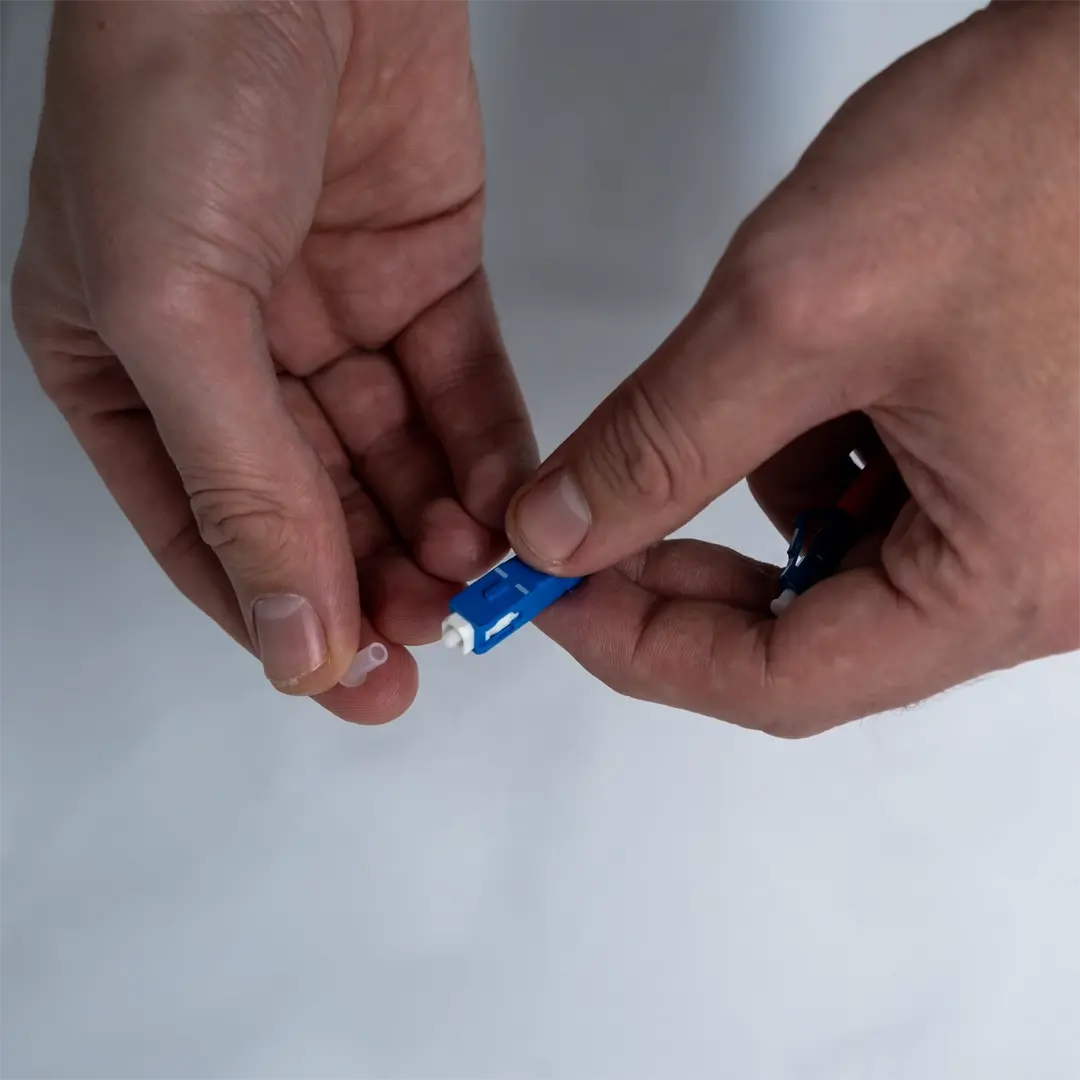 Henkilö poistaa läpinäkyvän suojatulpan sinisen valokuitukaapelin päästä.