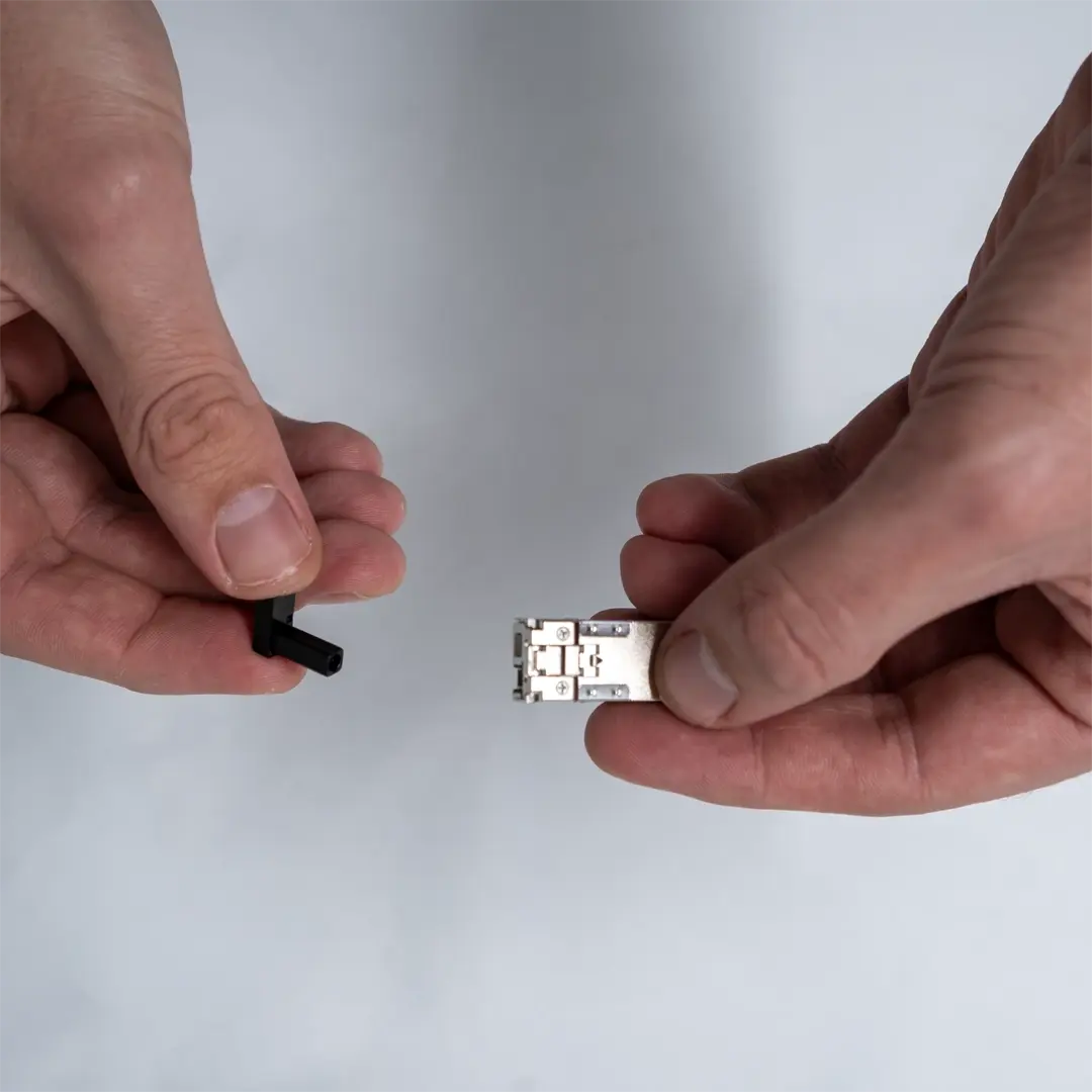 Henkilö pitää SFP-moduulia toisessa kädessä ja poistaa mustan suojatulpan toisella kädellä.