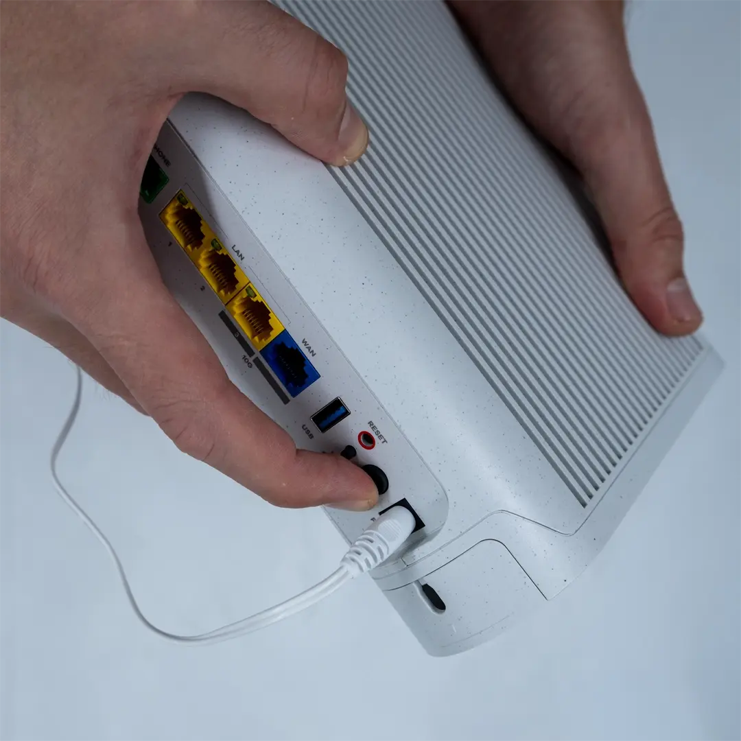 Henkilö painaa reitittimen takana olevaa virtapainiketta sen jälkeen, kun virtajohto on liitetty pistorasiaan.