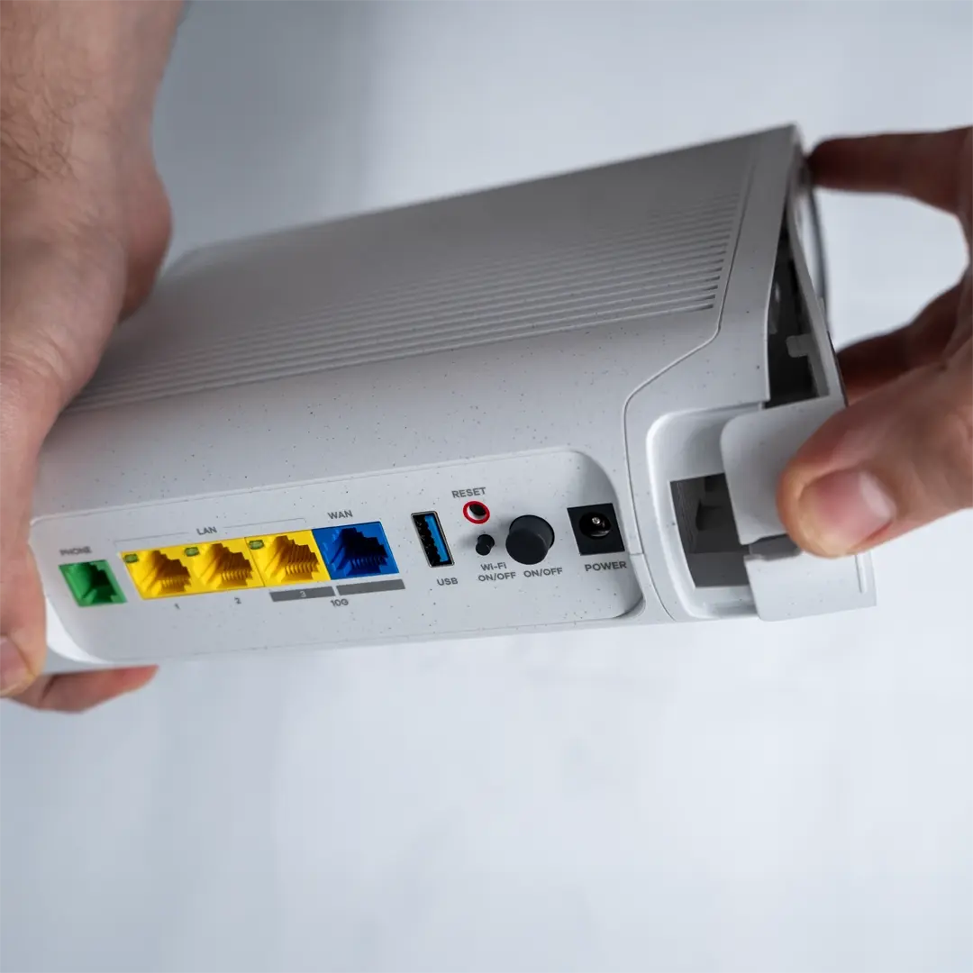 Henkilö irrottaa varovasti reitittimen pohjapaneelin vetämällä reunasta.
