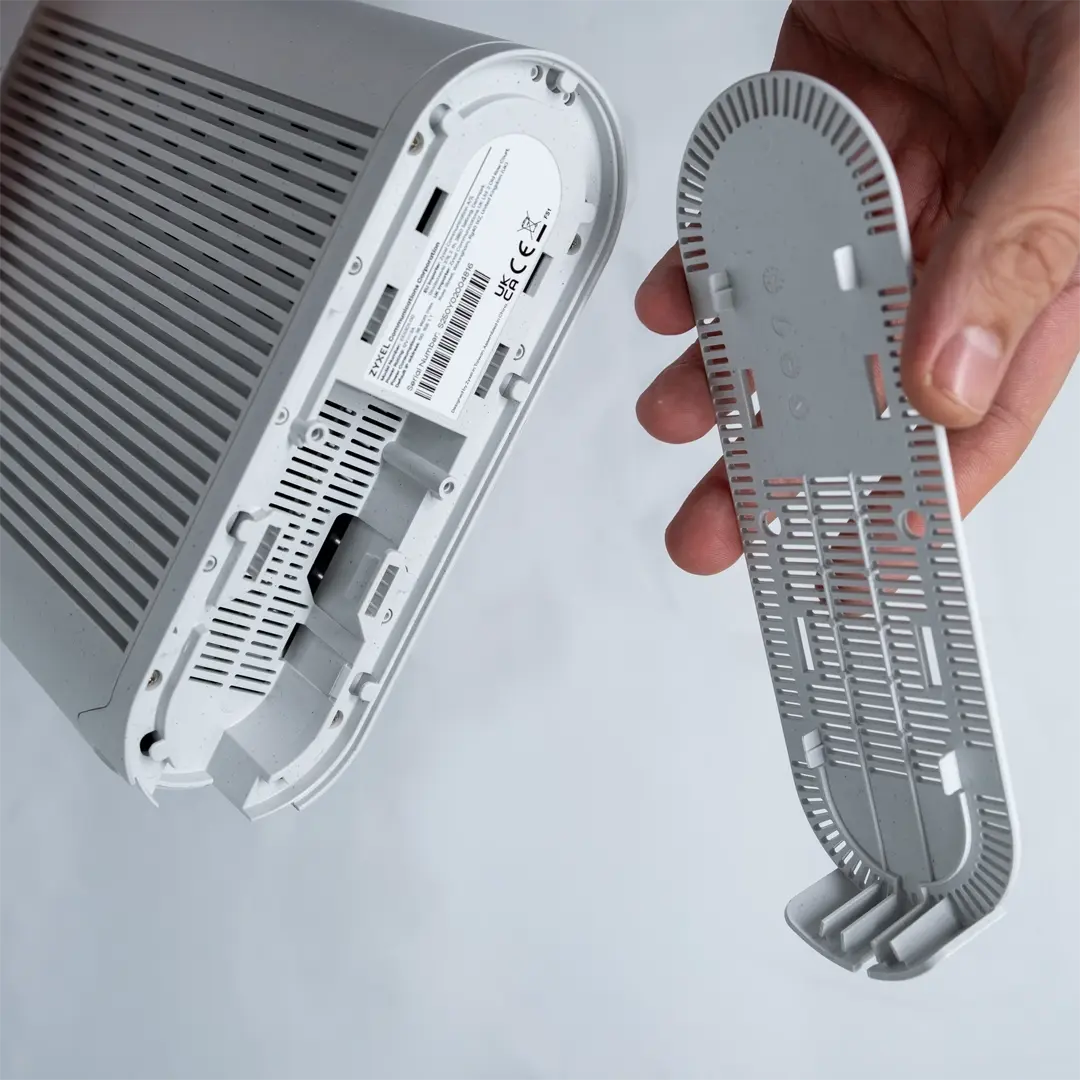 Henkilö on poistanut reitittimen pohjapaneelin ja pitää sitä laitteen vieressä siten, että laitteen pohjassa olevat liitännät näkyvät.